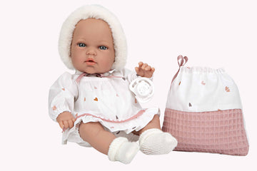 Muñeca Elegance Natal de Arias de 30 centímetros con conjunto blanco y rosa sentada al lado de su bolsa multiusos.