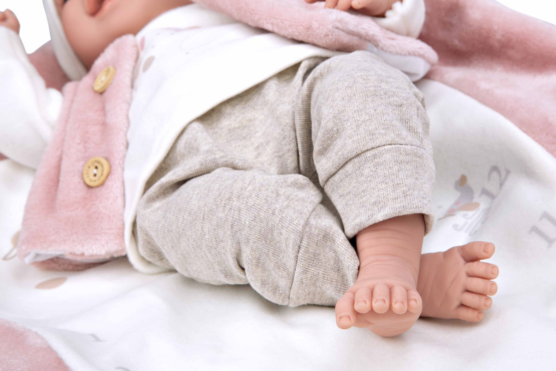 Primer plano de los pies realistas de la muñeca de peso de Arias vistiendo patucos rosa artesanales con lazo.