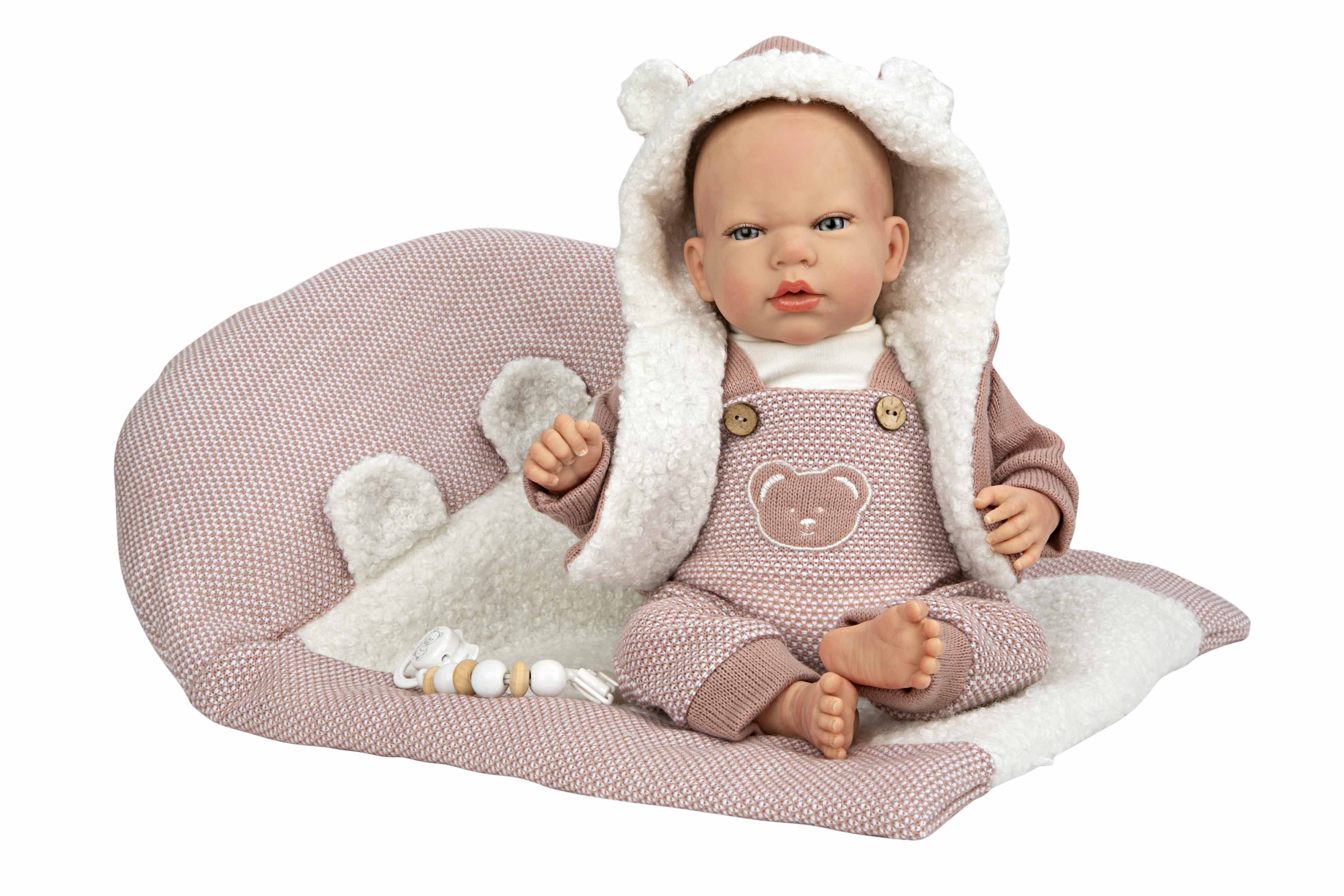 Muñeca Reborn Gadea de Arias de cuarenta centímetros con conjunto rosa de punto sentada en su cojín nido blanco.