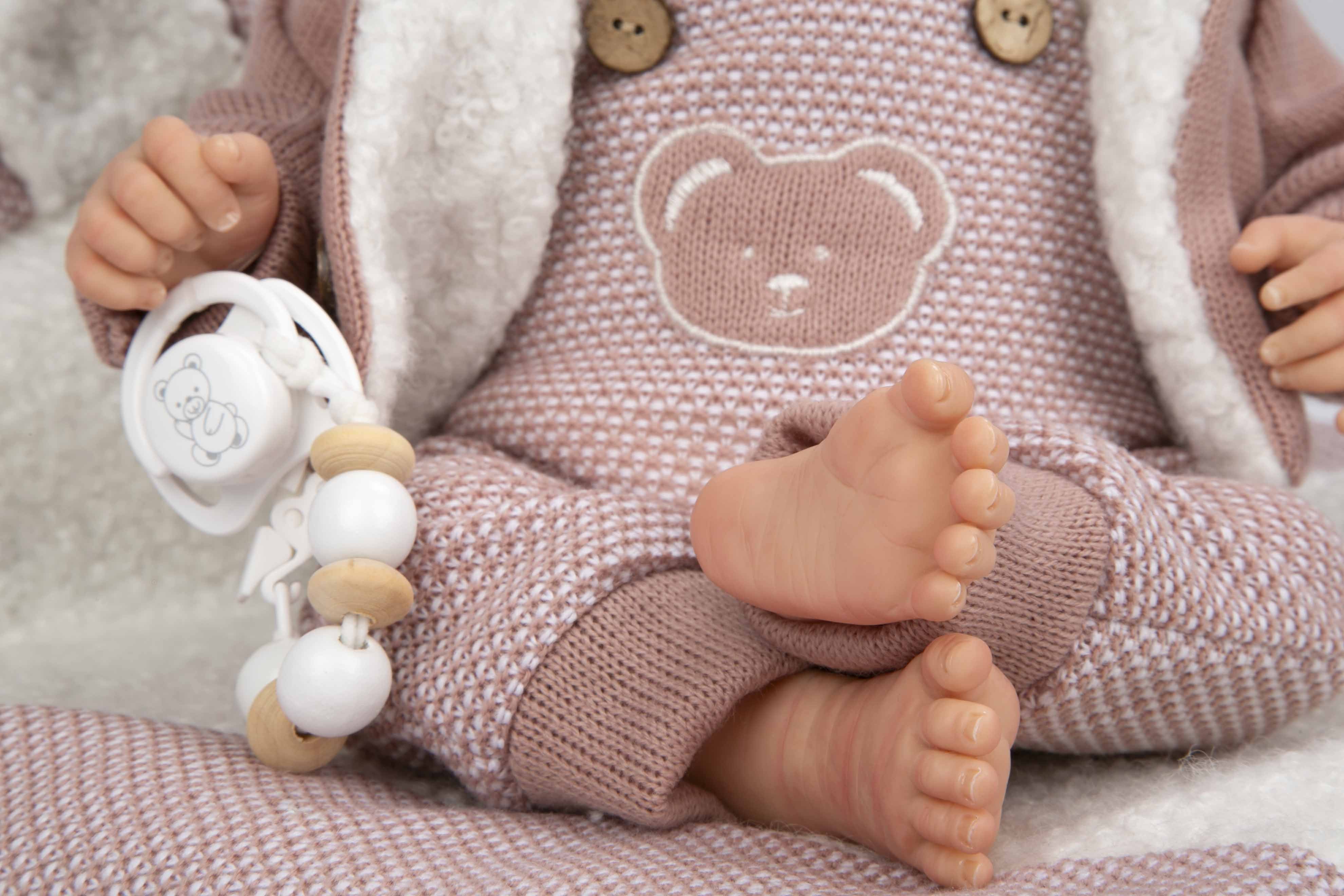 Muñeca Reborn articulada Gadea de Arias sentada de lado con su jersey rosa, garantizando un desarrollo real sin pantalla.