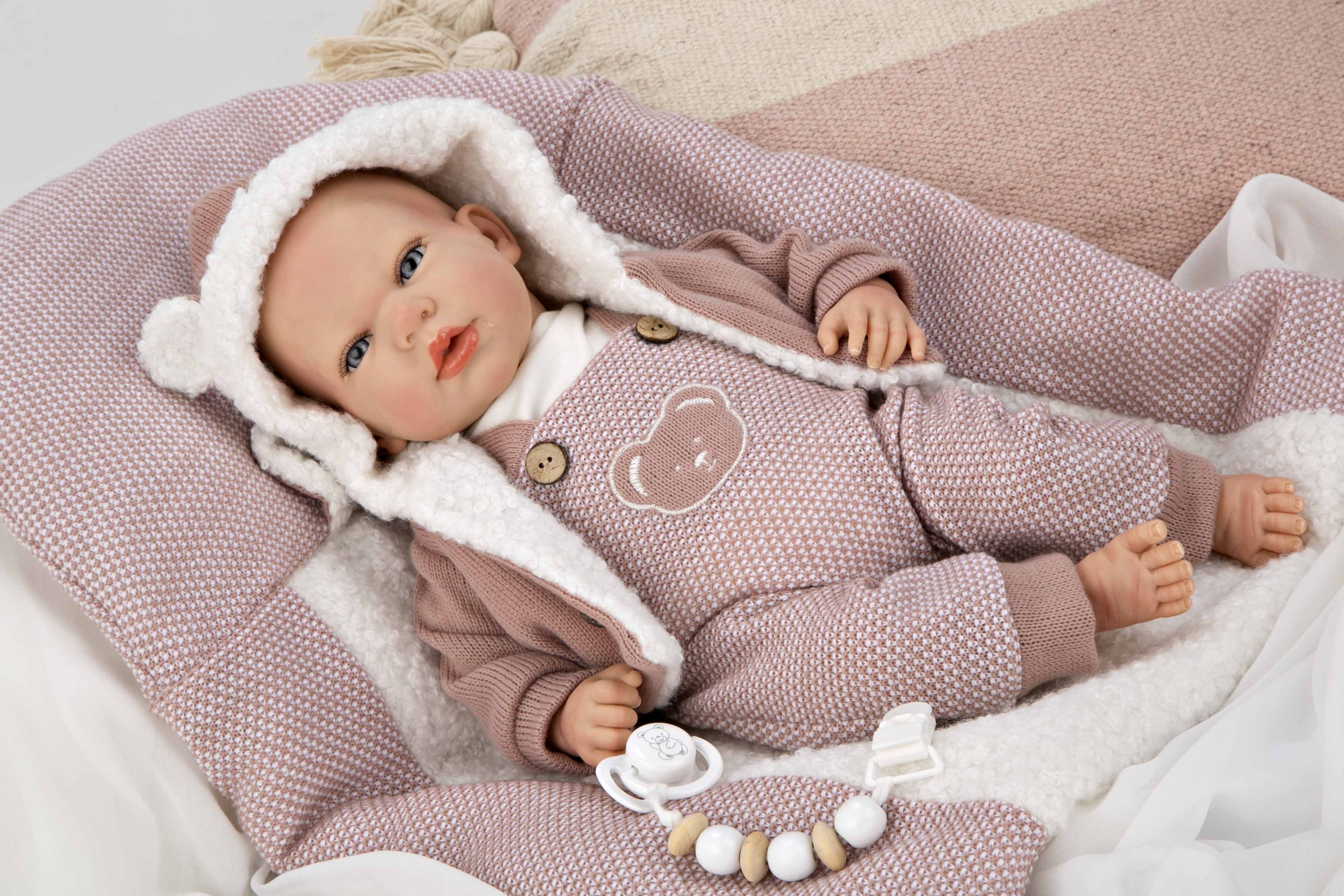 Muñeca Reborn Gadea de Muñecas Arias de espaldas enseñando la confección y cierres de su pelele rosa de alta calidad.
