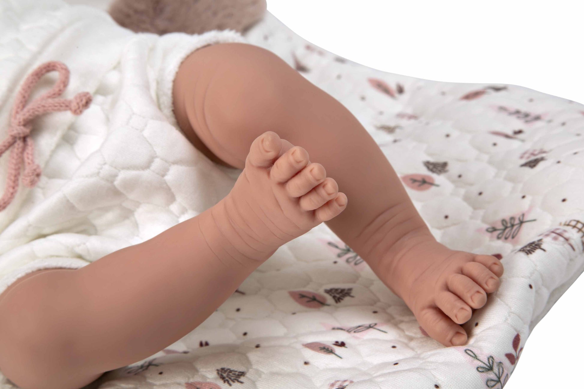 Primer plano de los pies de vinilo de la muñeca de Arias enseñando sus arrugas naturales y patucos de punto con lazo.