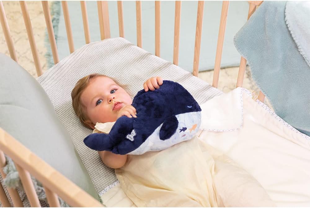 "Bebé en cuna usando el peluche ballena térmica Kaloo para aliviar cólicos y favorecer el sueño"