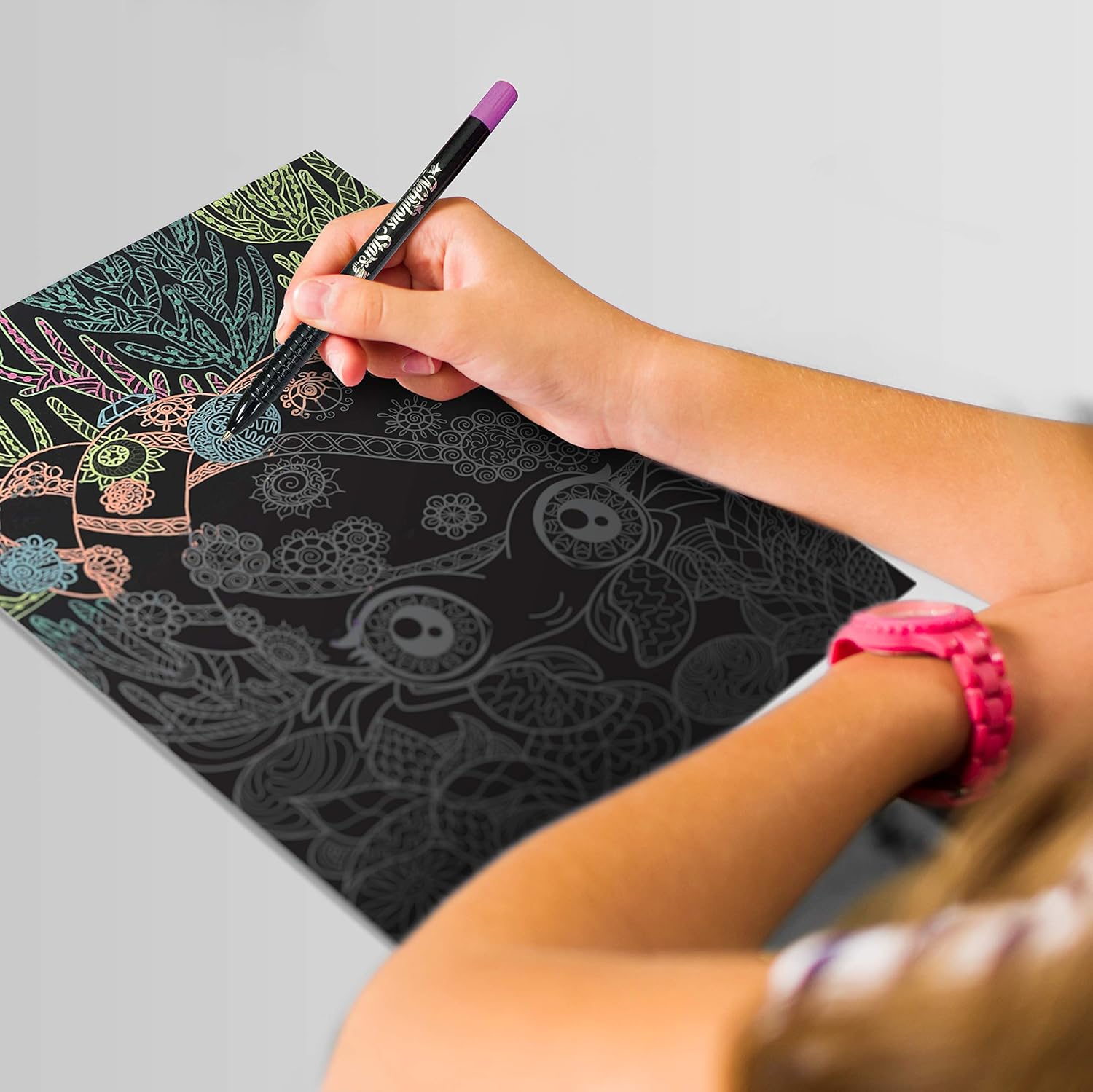 Niña utilizando los bolígrafos neón sobre el papel negro del cuaderno de bocetos Nebulous Stars.