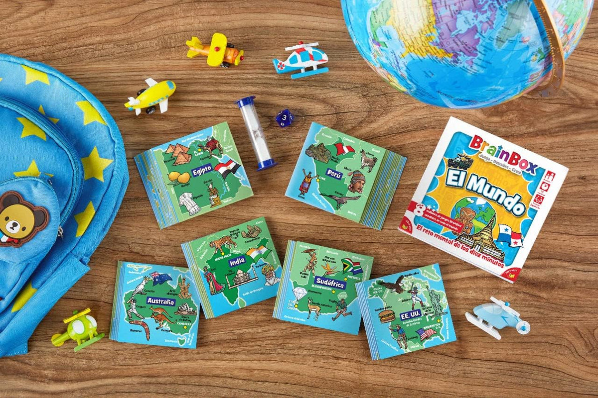 BrainBox El Mundo con tarjetas de países, caja, reloj de arena y dado sobre una mesa de madera junto a un globo terráqueo.