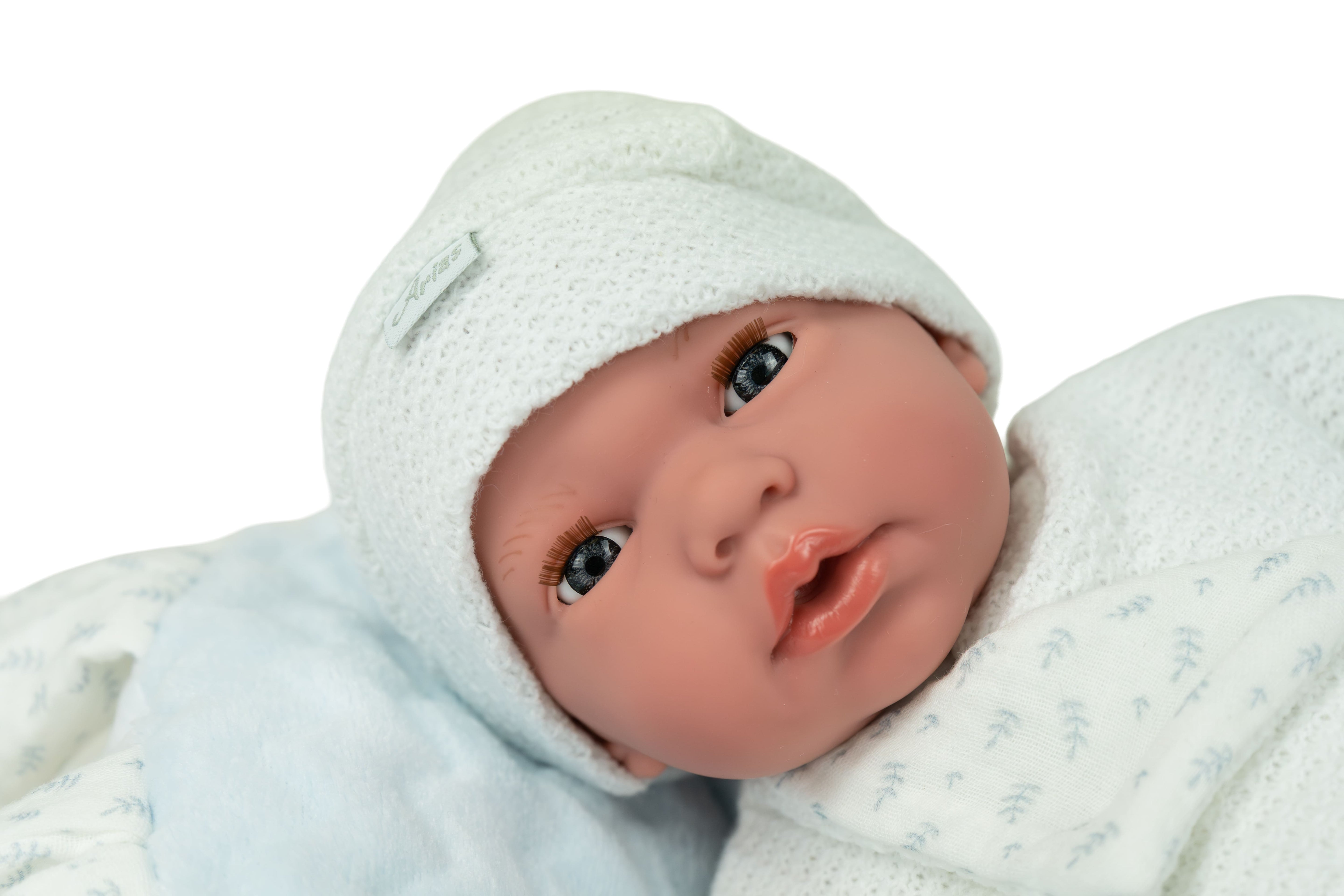 Primer plano del rostro de la muñeca bebé Andie Muñecas Arias, ojos azules durmientes abiertos, gorrito blanco y expresión realista