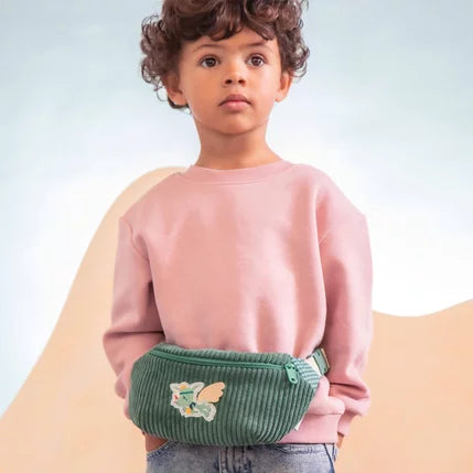 Niño con jersey rosa llevando la riñonera verde Joe el Dragón de Lilliputiens alrededor de la cintura.